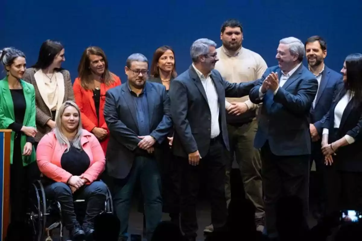 Un grupo de personas vestidas formalmente posando en un escenario mientras algunas sonríen y otras aplauden