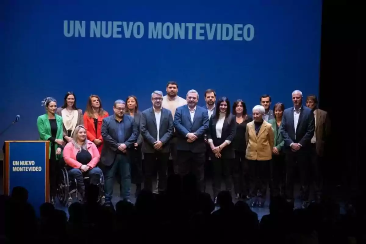 Un grupo de personas posando en un escenario con fondo azul y el texto UN NUEVO MONTEVIDEO Un grupo de personas posando en un escenario con fondo azul y el texto UN NUEVO MONTEVIDEO