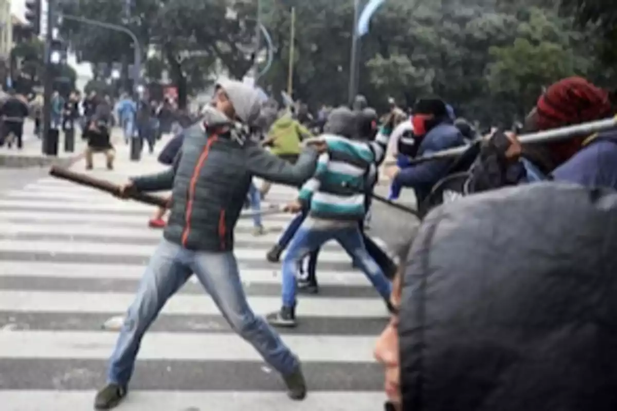 Personas participando en una manifestación en la calle, algunas con el rostro cubierto y sosteniendo objetos. Personas participando en una manifestación en la calle, algunas con el rostro cubierto y sosteniendo objetos.