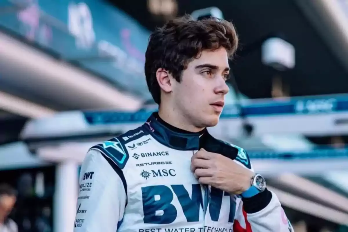 Joven piloto de automovilismo con traje de carreras blanco y azul ajustándose el cuello en un paddock de Fórmula 1
