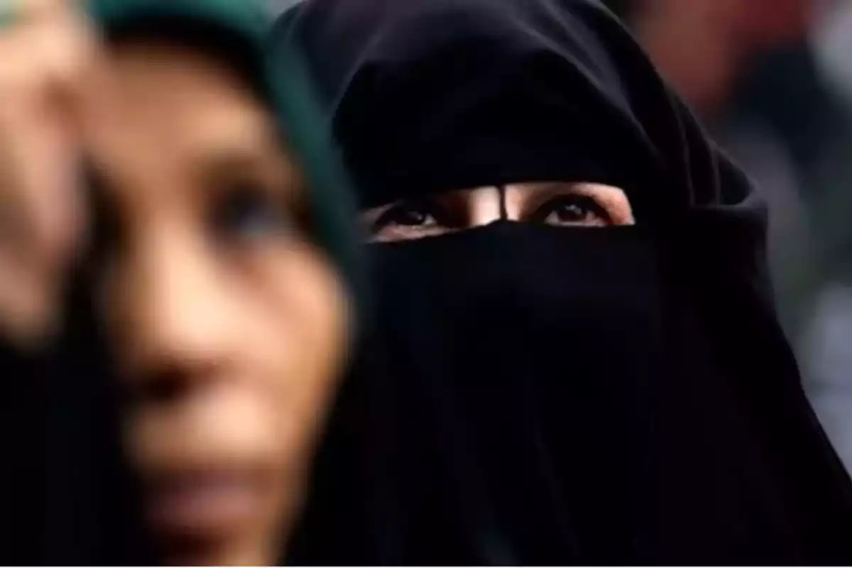 Mujer con velo negro cubriendo su rostro y otra figura desenfocada en primer plano Mujer con velo negro cubriendo su rostro y otra figura desenfocada en primer plano