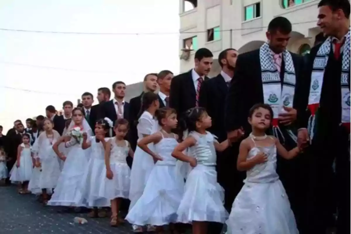 Un grupo de hombres y niñas vestidas de blanco caminan en fila durante un evento al aire libre.