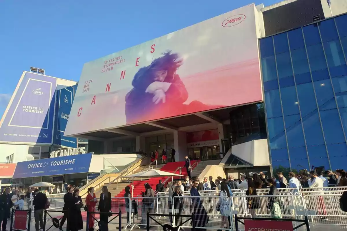 Fachada del Palacio de Festivales de Cannes con una gran lona promocional del Festival de Cine y una multitud de personas esperando en la entrada sobre la alfombra roja Fachada del Palacio de Festivales de Cannes con una gran lona promocional del Festival de Cine y una multitud de personas esperando en la entrada sobre la alfombra roja