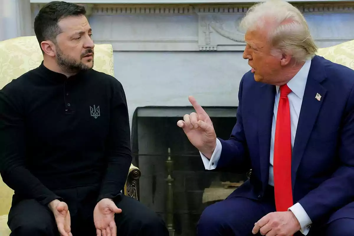Two men sitting in a room, one in a dark suit and red tie gesturing with his hand, while the other, in a black sweater, watches him intently. Two men sitting in a room, one in a dark suit and red tie gesturing with his hand, while the other, in a black sweater, watches him intently.