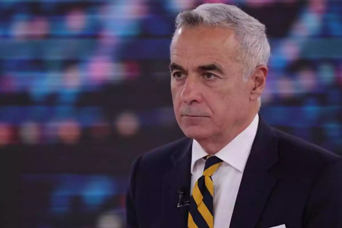 Gray-haired man in a dark suit and striped tie in a studio setting with a blurred background.