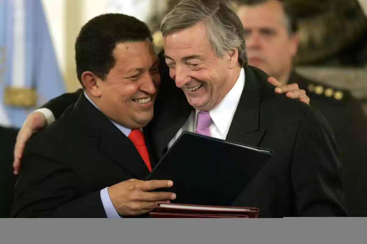 Dos personas sonrientes se abrazan mientras sostienen un documento en un entorno formal.