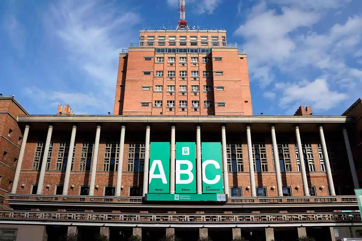 Edificio de ladrillo con columnas y un cartel verde grande que dice ABC.