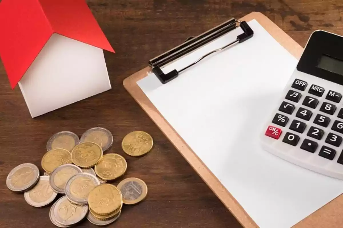 A calculator, coins, a clipboard, and a miniature house on a wooden table. A calculator, coins, a clipboard, and a miniature house on a wooden table.