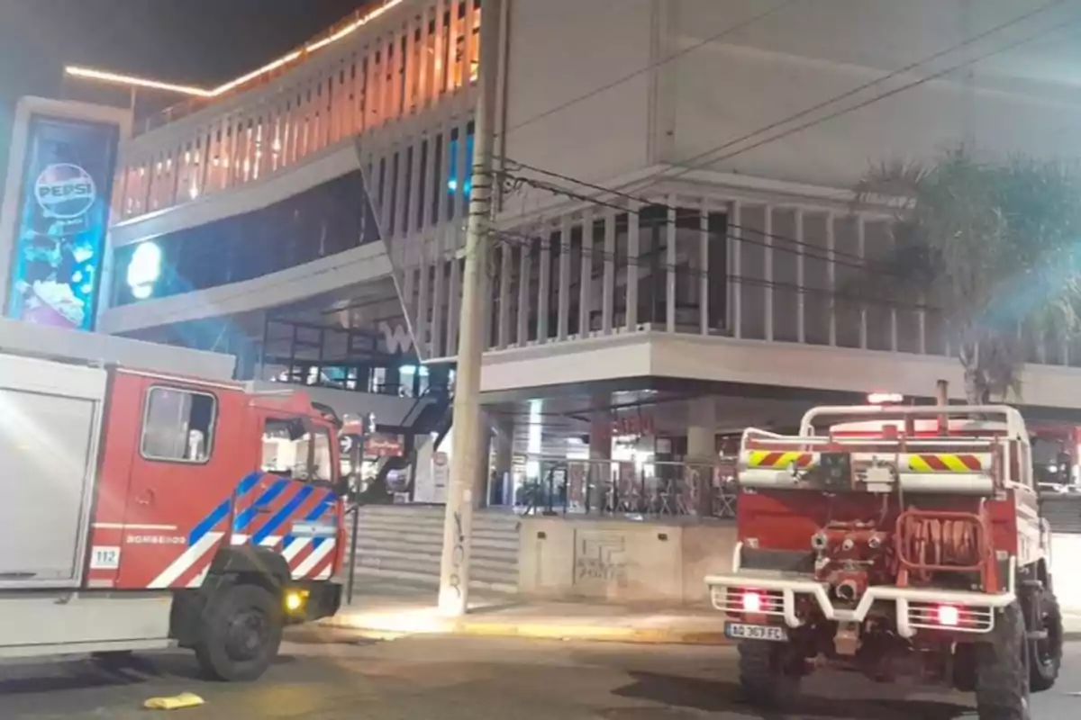 Dos camiones de bomberos estacionados frente a un edificio moderno iluminado por la noche