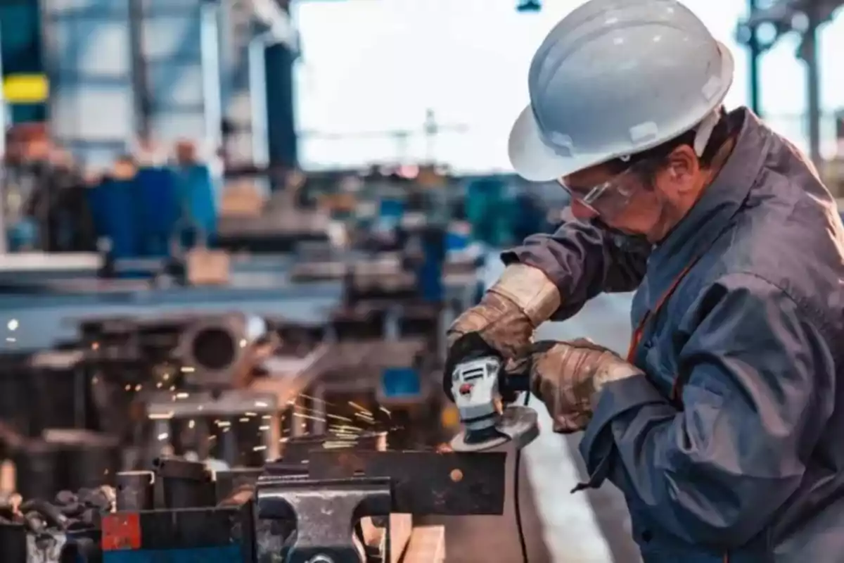 Trabajador con casco y gafas protectoras usando una herramienta eléctrica en un taller industrial.