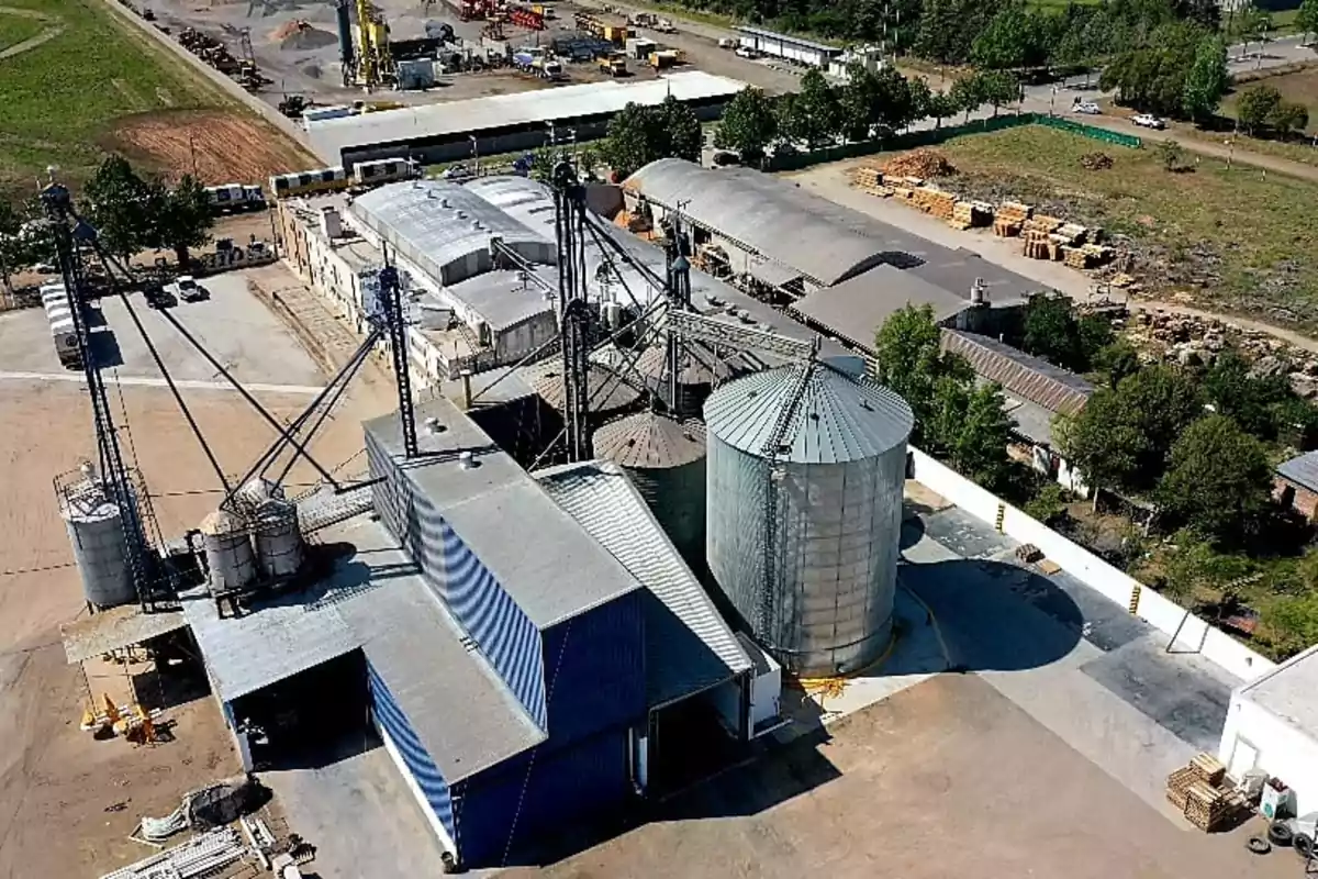 Vista aérea de una planta industrial con varios silos metálicos y edificios rodeados de áreas verdes y maquinaria Vista aérea de una planta industrial con varios silos metálicos y edificios rodeados de áreas verdes y maquinaria