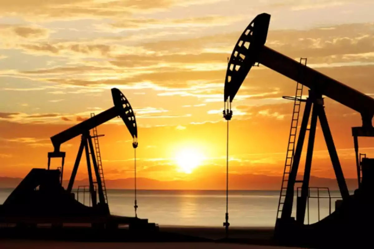 Máquinas de extracción de petróleo en silueta al atardecer con un cielo anaranjado y el sol en el horizonte.