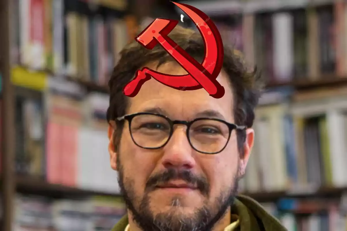 Un hombre con gafas y barba frente a una estantería de libros con un símbolo de hoz y martillo en la frente.