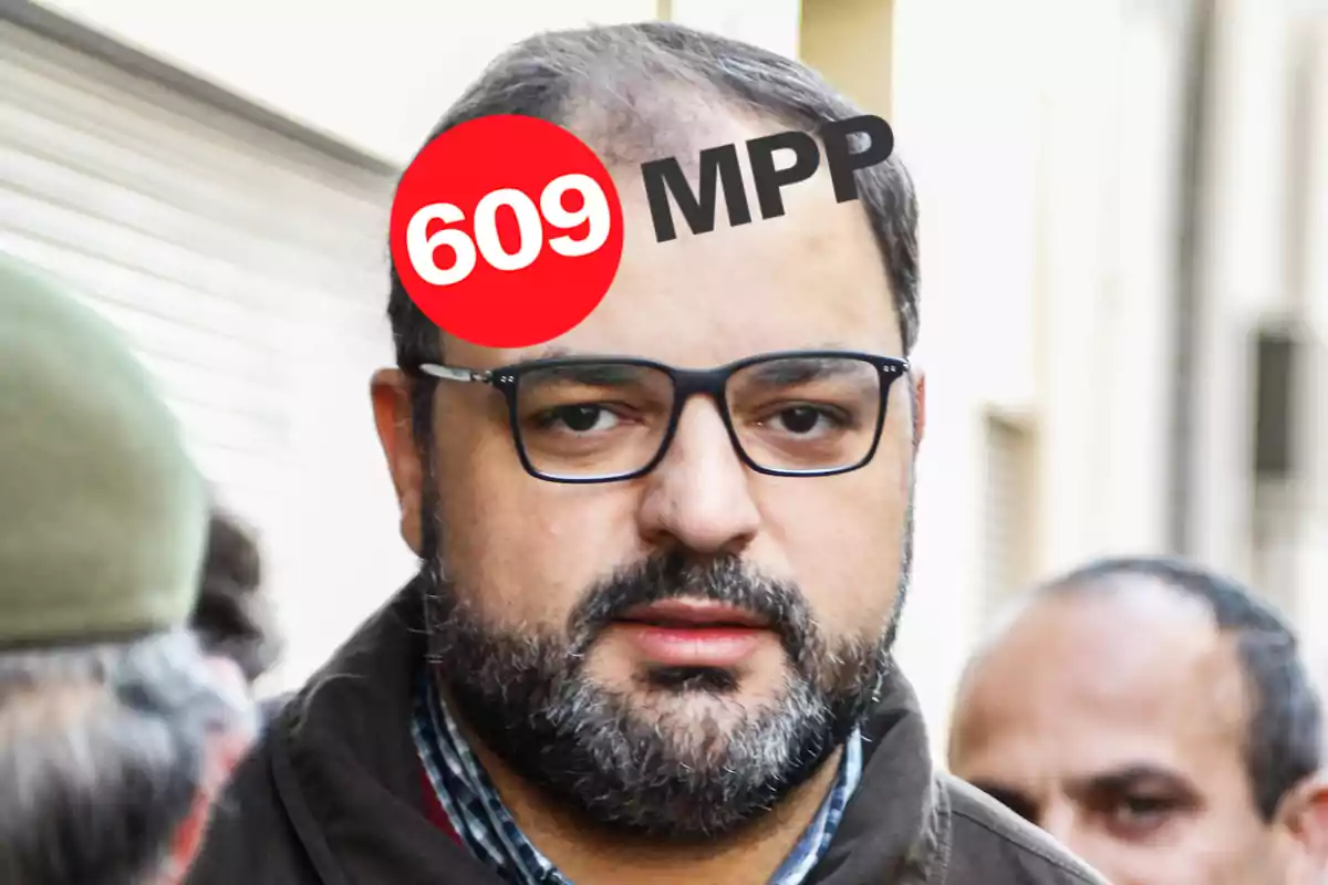 Hombre con barba y gafas, con un círculo rojo en la frente que tiene el número 609 y las letras MPP