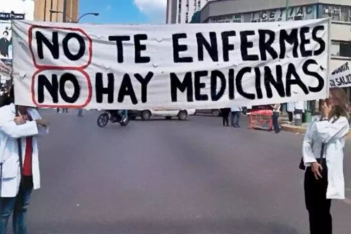 Personas con batas blancas sostienen una pancarta que dice "No te enfermes, no hay medicinas" en una calle.