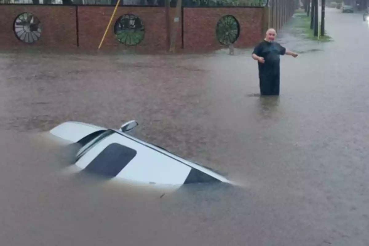 A man is standing on a flooded street while a car is partially submerged in the water. A man is standing on a flooded street while a car is partially submerged in the water.