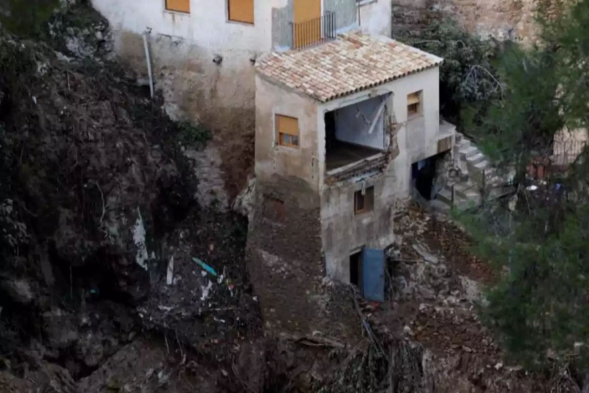 Una casa dañada en un acantilado con parte de su estructura colapsada y escombros alrededor.