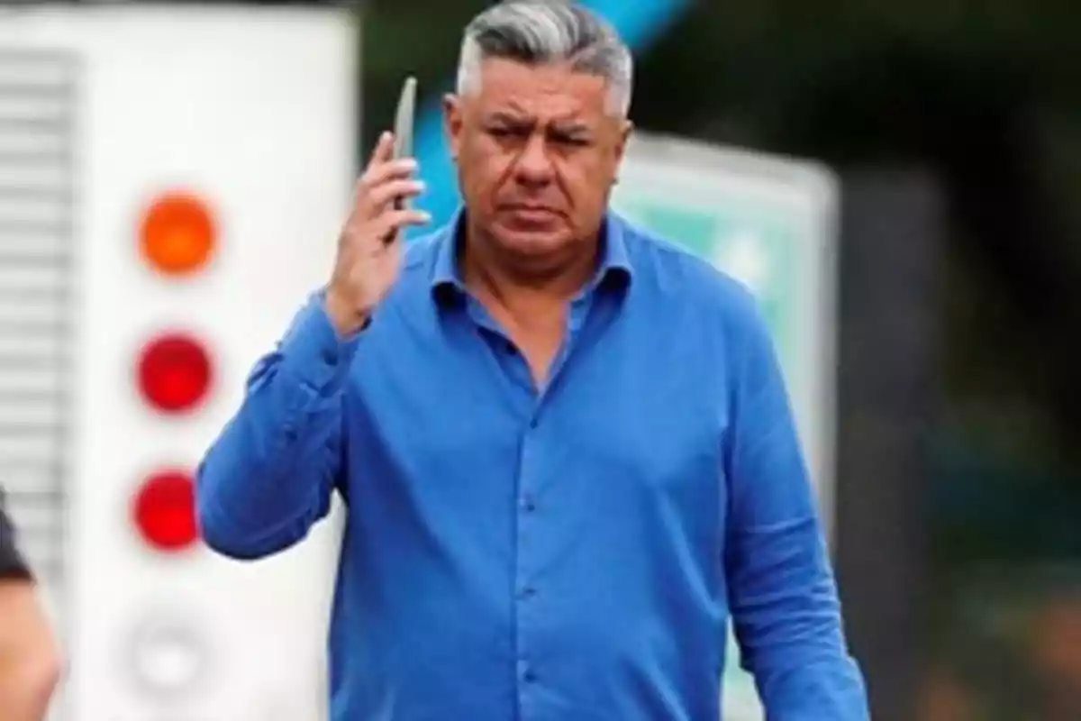 Hombre de cabello canoso y camisa azul sosteniendo un teléfono móvil cerca de su oído.