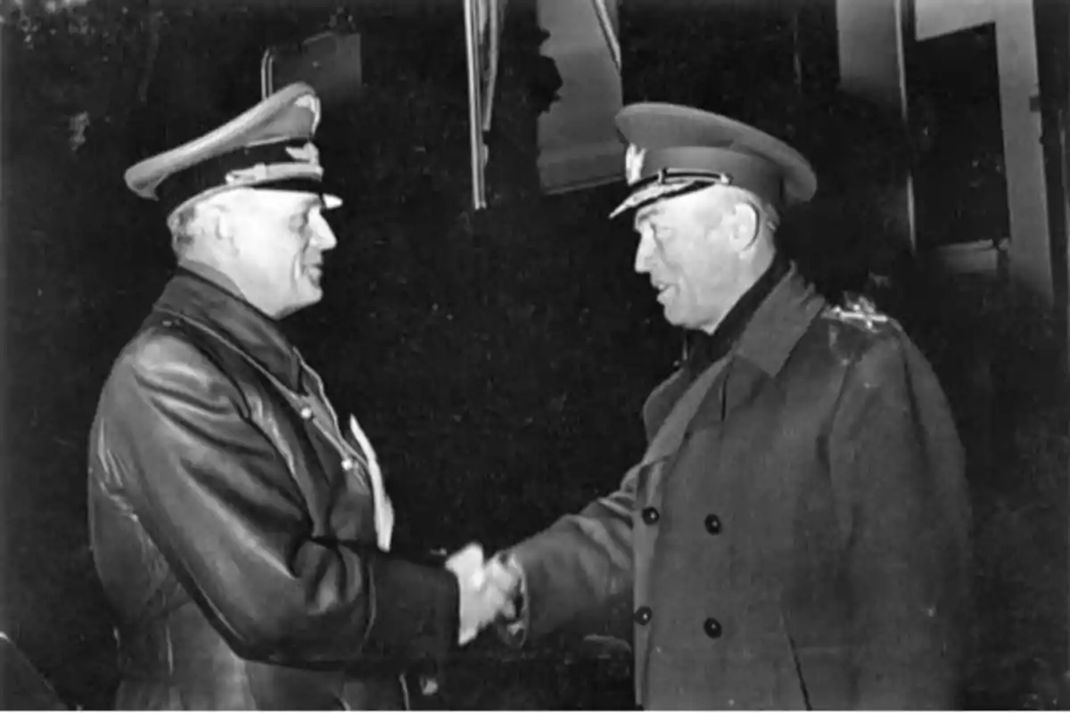 Two men in military uniforms shake hands in a black and white photograph. Two men in military uniforms shake hands in a black and white photograph.
