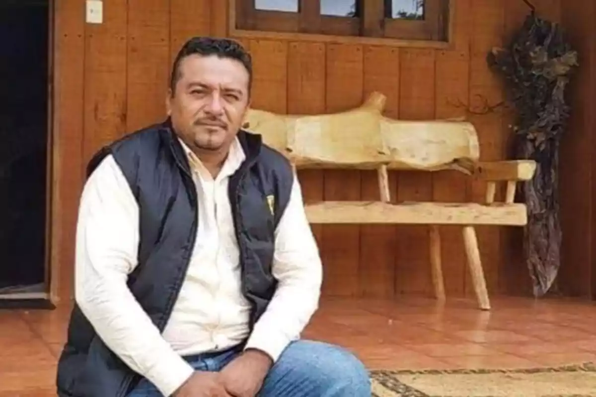 Un hombre sentado frente a una casa de madera con un banco rústico detrás. Un hombre sentado frente a una casa de madera con un banco rústico detrás.