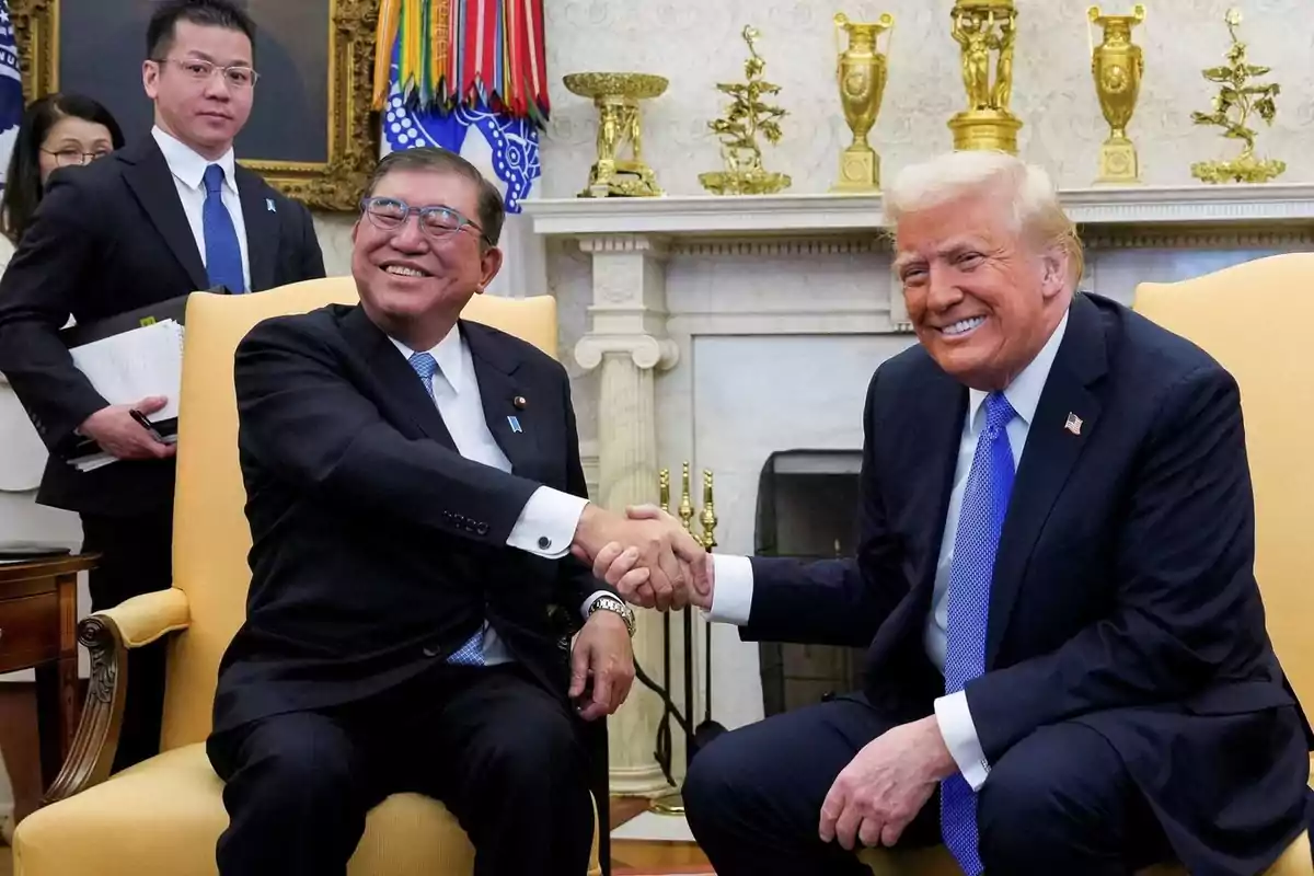 Two men in suits shake hands and smile while sitting in yellow armchairs in an elegant room with gold decorations and flags in the background. Two men in suits shake hands and smile while sitting in yellow armchairs in an elegant room with gold decorations and flags in the background.