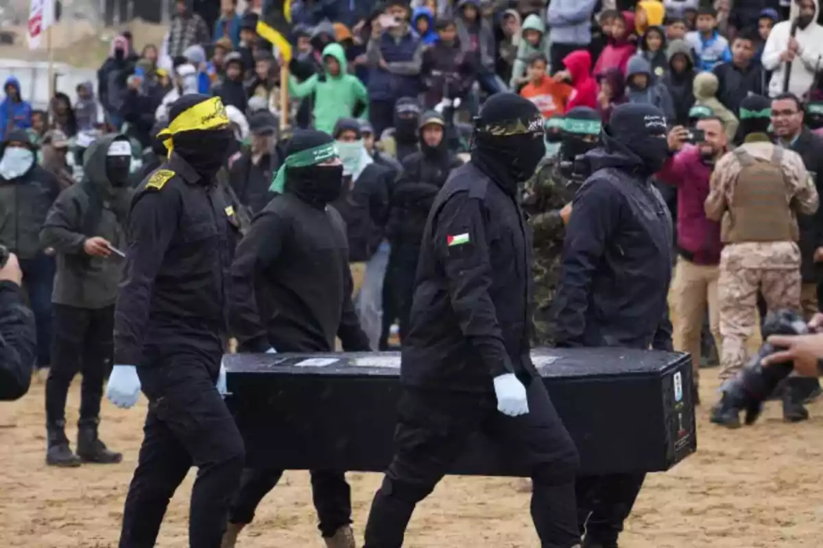 A group of people dressed in black with their faces covered is carrying a coffin in a crowded place.