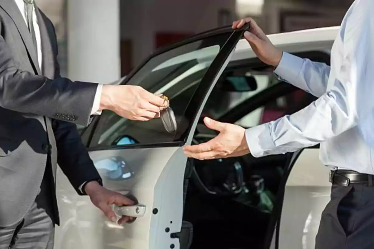 Two people exchanging car keys next to an open door. Two people exchanging car keys next to an open door.