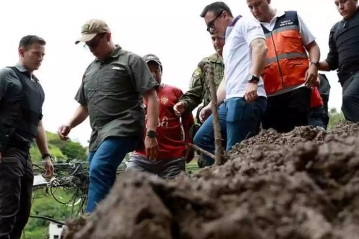 Un grupo de personas camina sobre un terreno lodoso, algunas llevan chalecos y uniformes.