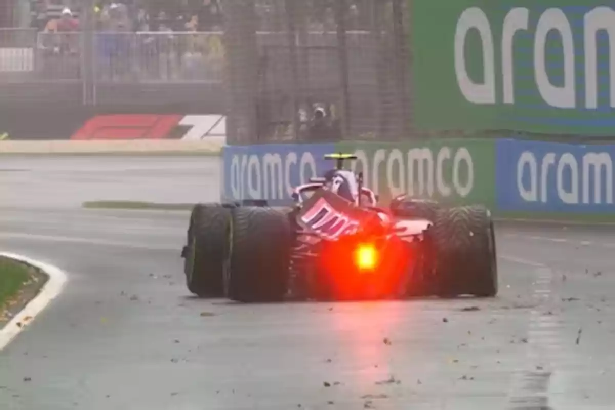 A race car on a wet track with taillights on and Aramco advertising in the background. A race car on a wet track with taillights on and Aramco advertising in the background.