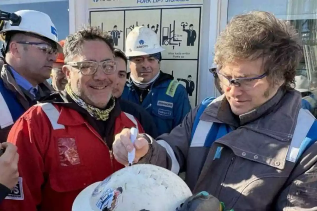 Un grupo de personas con cascos y equipo de seguridad en un entorno industrial, una de ellas firma un casco blanco.