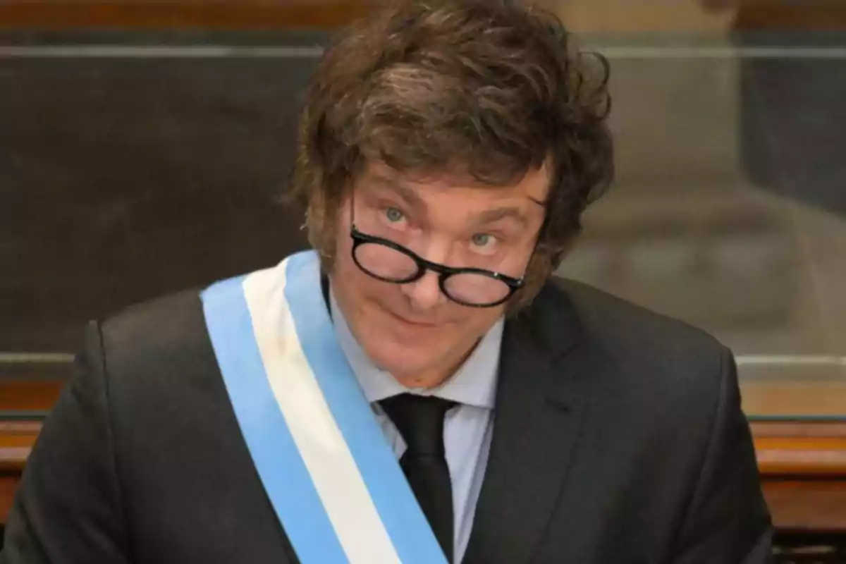 Un hombre con gafas y una banda presidencial en un entorno formal.