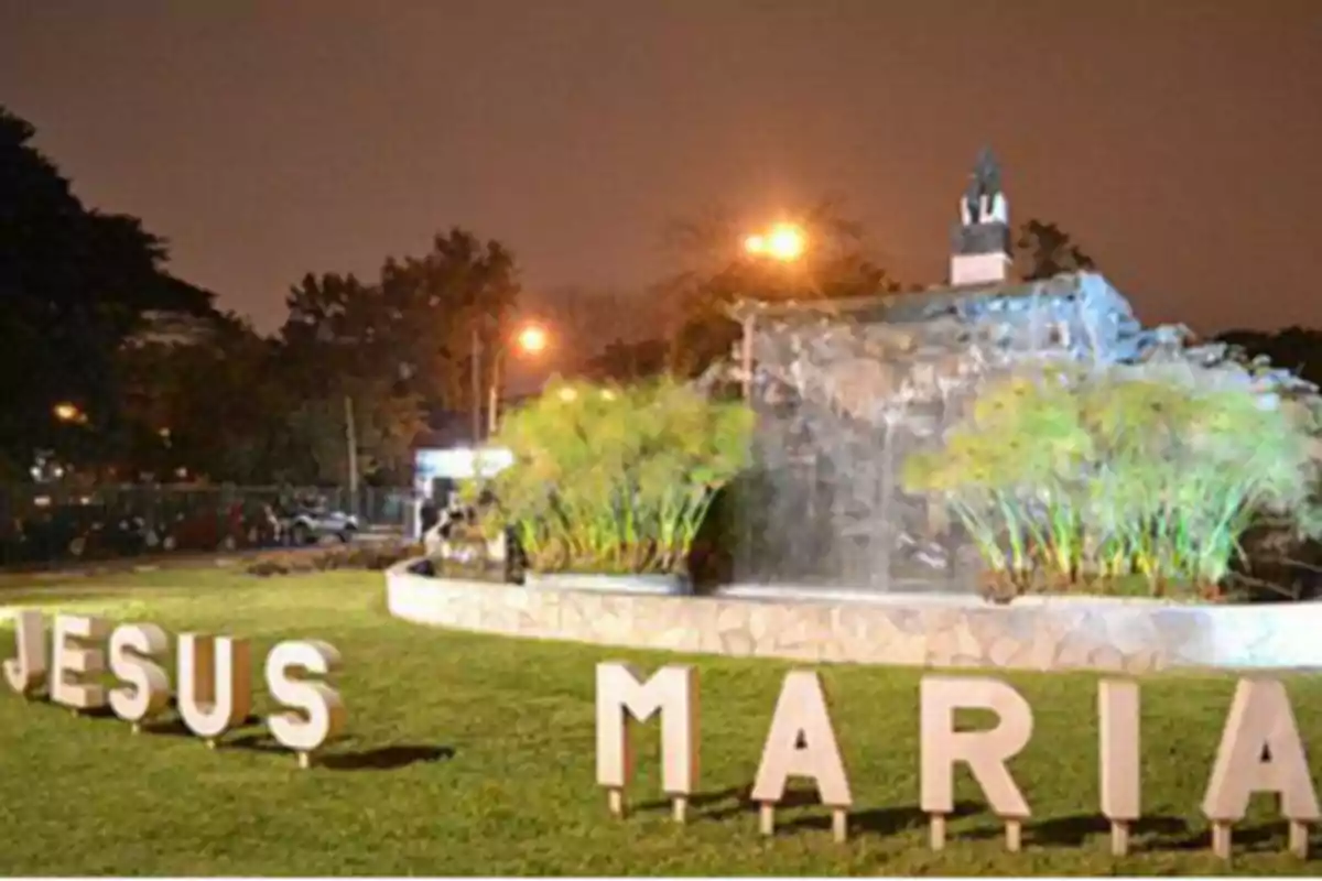 Letras grandes que forman el nombre Jesús María en un parque con césped y una fuente iluminada por la noche Letras grandes que forman el nombre Jesús María en un parque con césped y una fuente iluminada por la noche