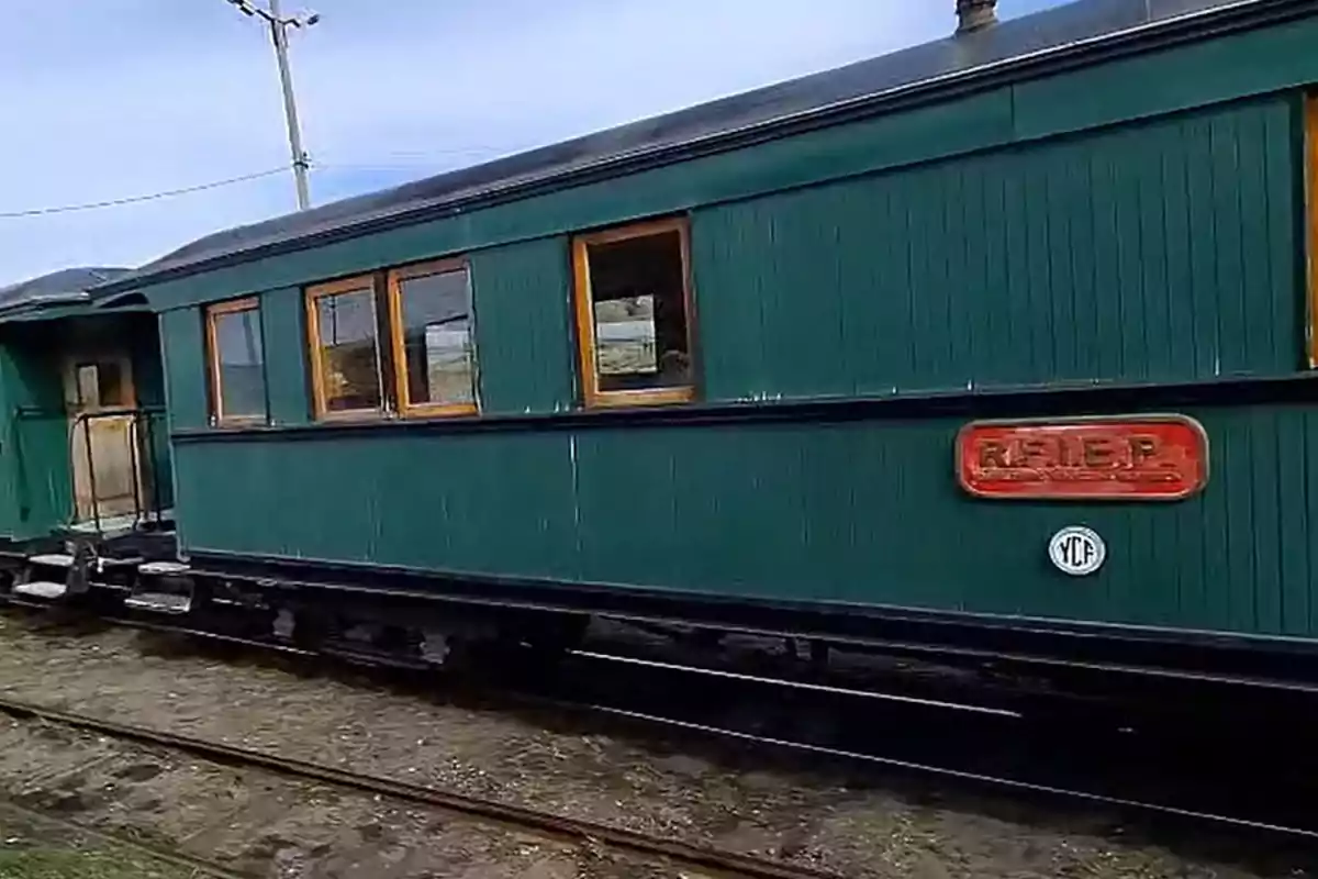 Un vagón de tren antiguo de color verde con ventanas de madera y un letrero rojo en el costado.