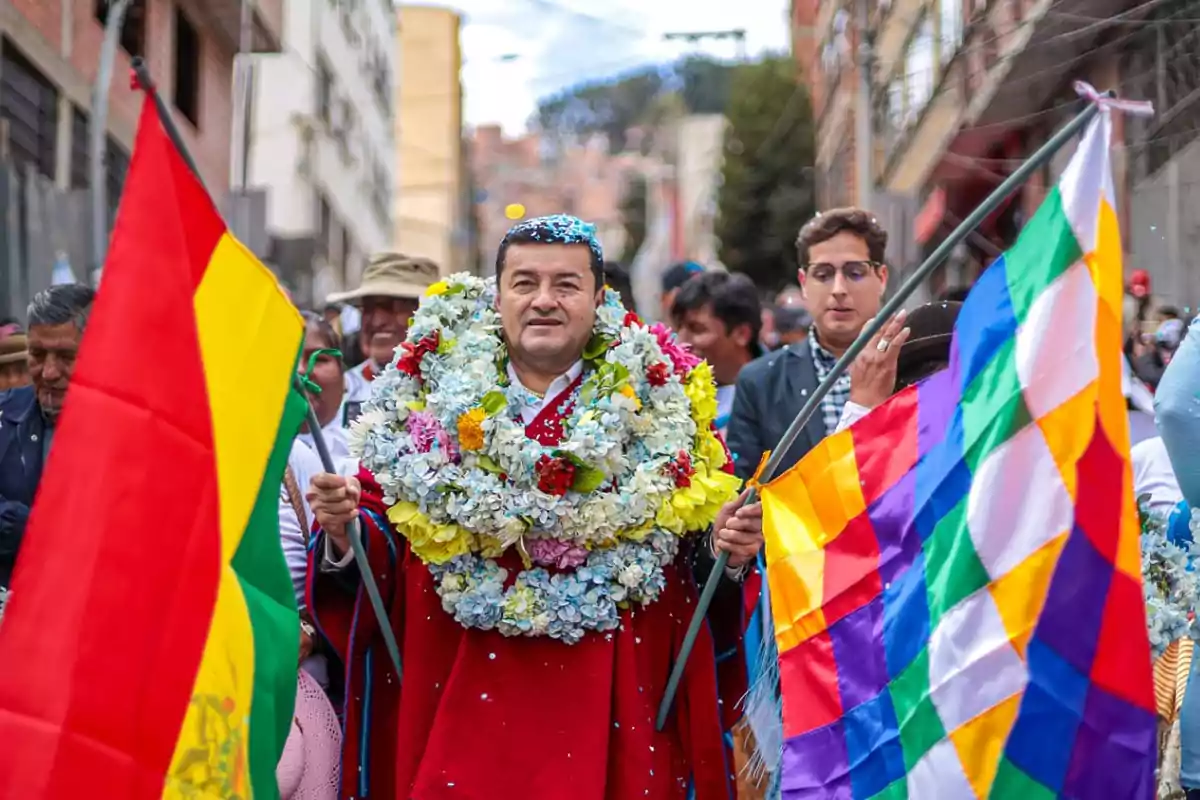 Man with a flower garland surrounded by people on a street, holding Bolivian and Wiphala flags during a celebration Man with a flower garland surrounded by people on a street, holding Bolivian and Wiphala flags during a celebration