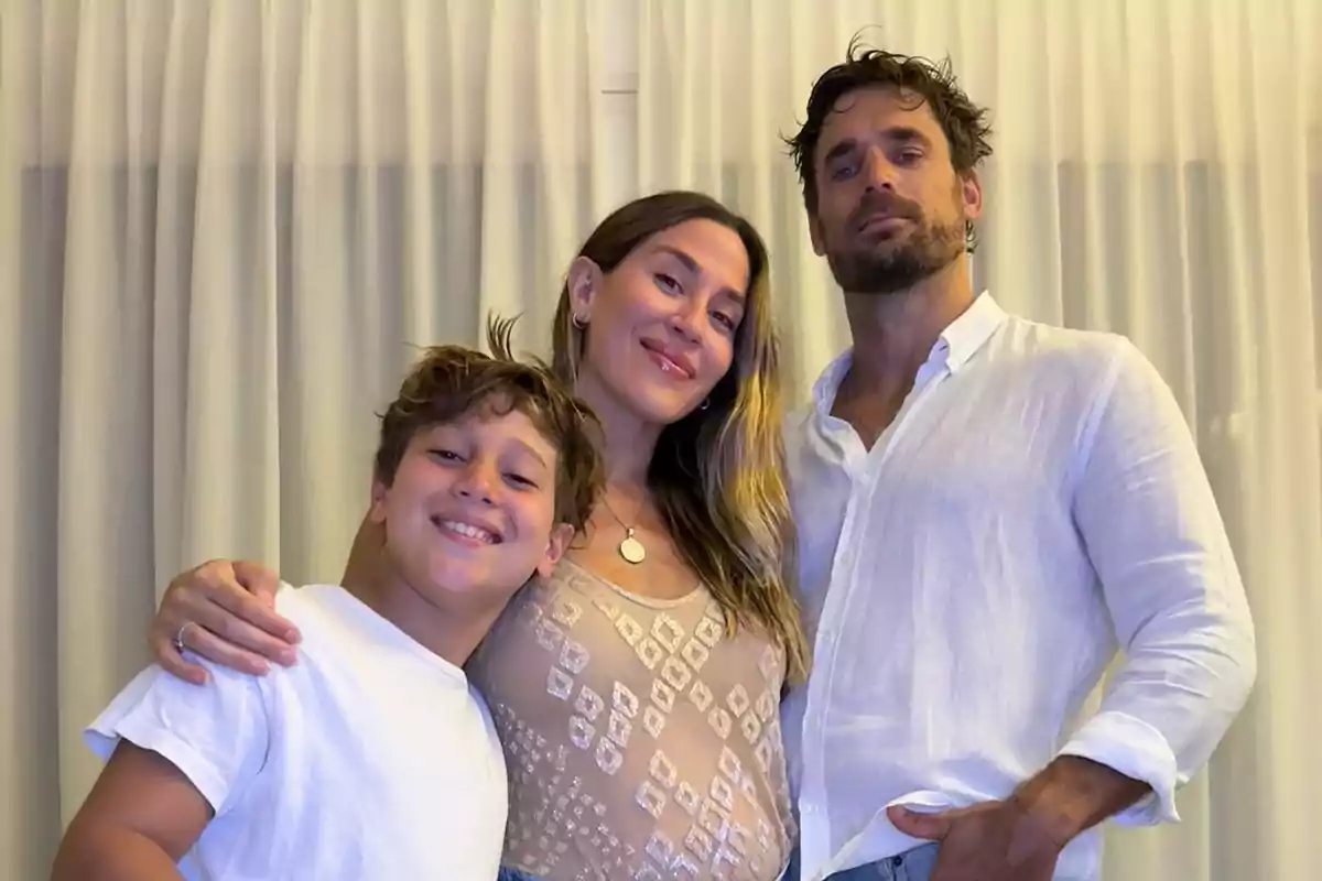 Una familia sonriente posando frente a una cortina blanca.