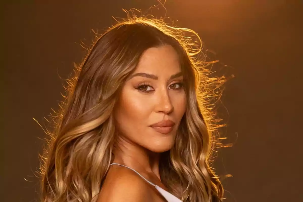Mujer de cabello largo y ondulado con luz cálida de fondo mirando hacia la cámara