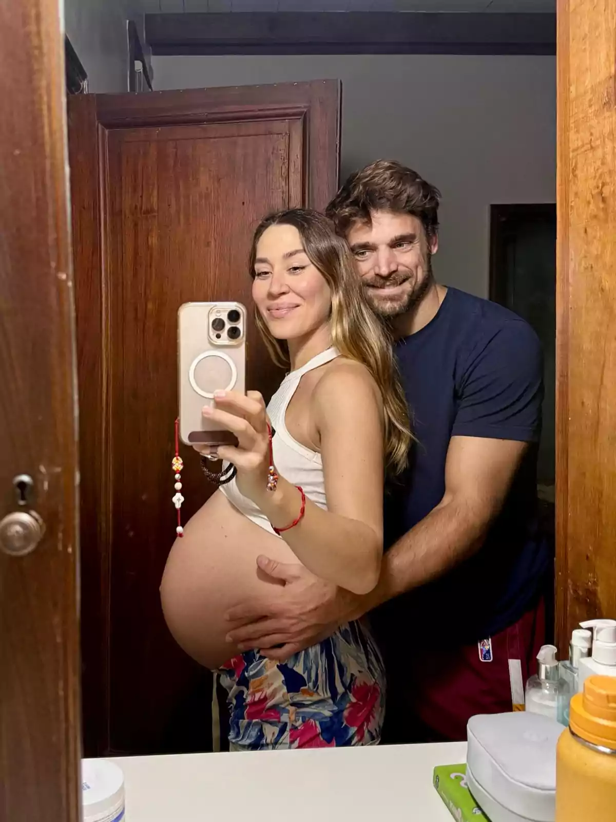 A smiling couple takes a selfie in the bathroom mirror, the woman is pregnant and the man is lovingly embracing her. A smiling couple takes a selfie in the bathroom mirror, the woman is pregnant and the man is lovingly embracing her.