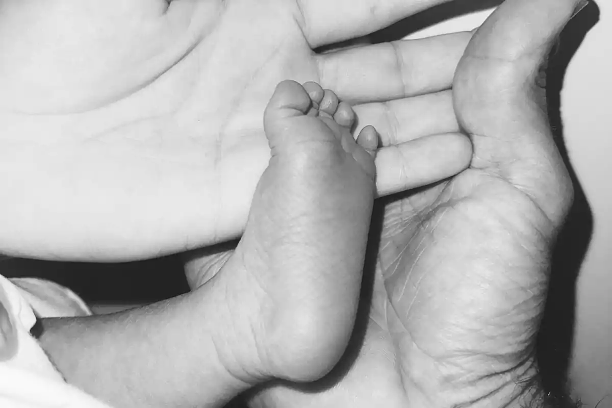 Mano de adulto sosteniendo la mano de un niño y el pie de un bebé en blanco y negro Mano de adulto sosteniendo la mano de un niño y el pie de un bebé en blanco y negro