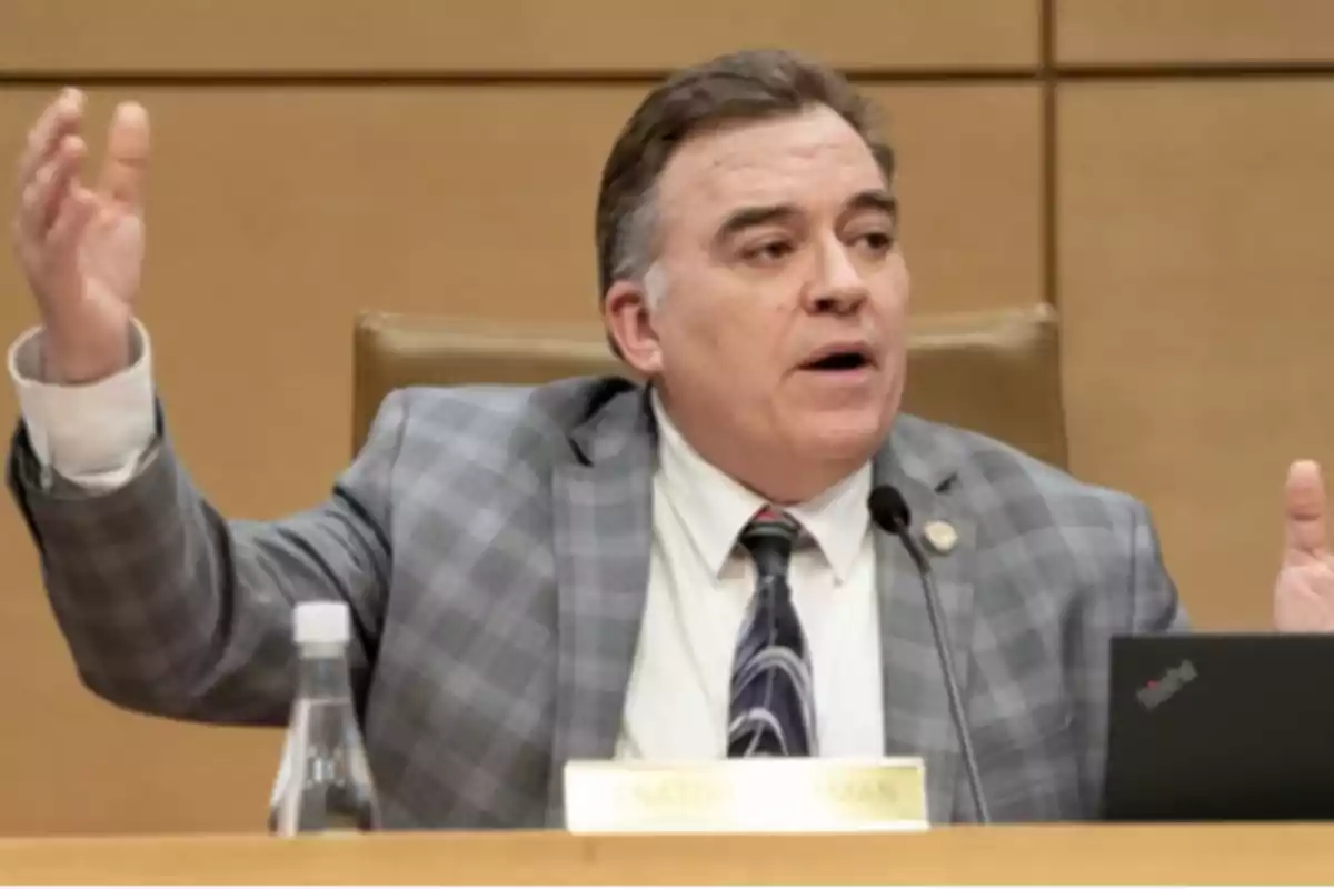 Middle-aged man in a checkered jacket speaking at a meeting while gesturing with his hands and with a microphone in front of him Middle-aged man in a checkered jacket speaking at a meeting while gesturing with his hands and with a microphone in front of him