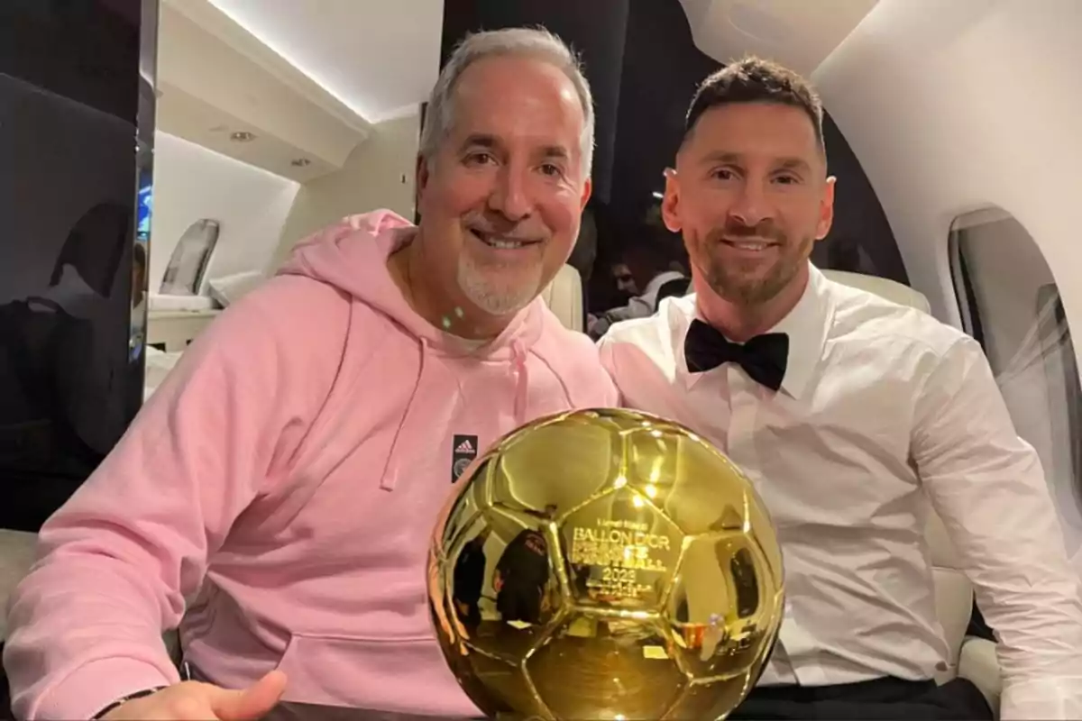 Dos personas sonríen mientras posan sentadas en un avión privado sosteniendo un trofeo dorado de Balón de Oro Dos personas sonríen mientras posan sentadas en un avión privado sosteniendo un trofeo dorado de Balón de Oro