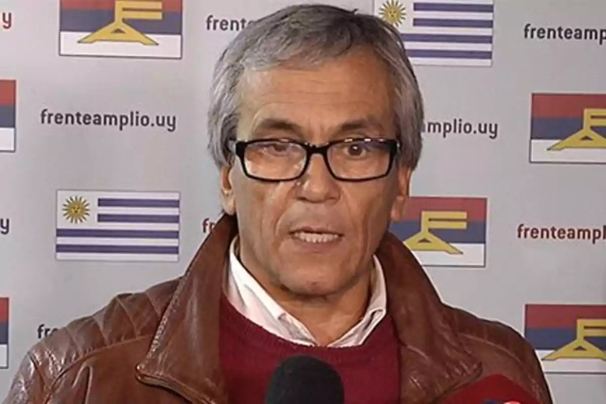 Hombre de cabello canoso y gafas hablando frente a un fondo con banderas de Uruguay y del Frente Amplio Hombre de cabello canoso y gafas hablando frente a un fondo con banderas de Uruguay y del Frente Amplio