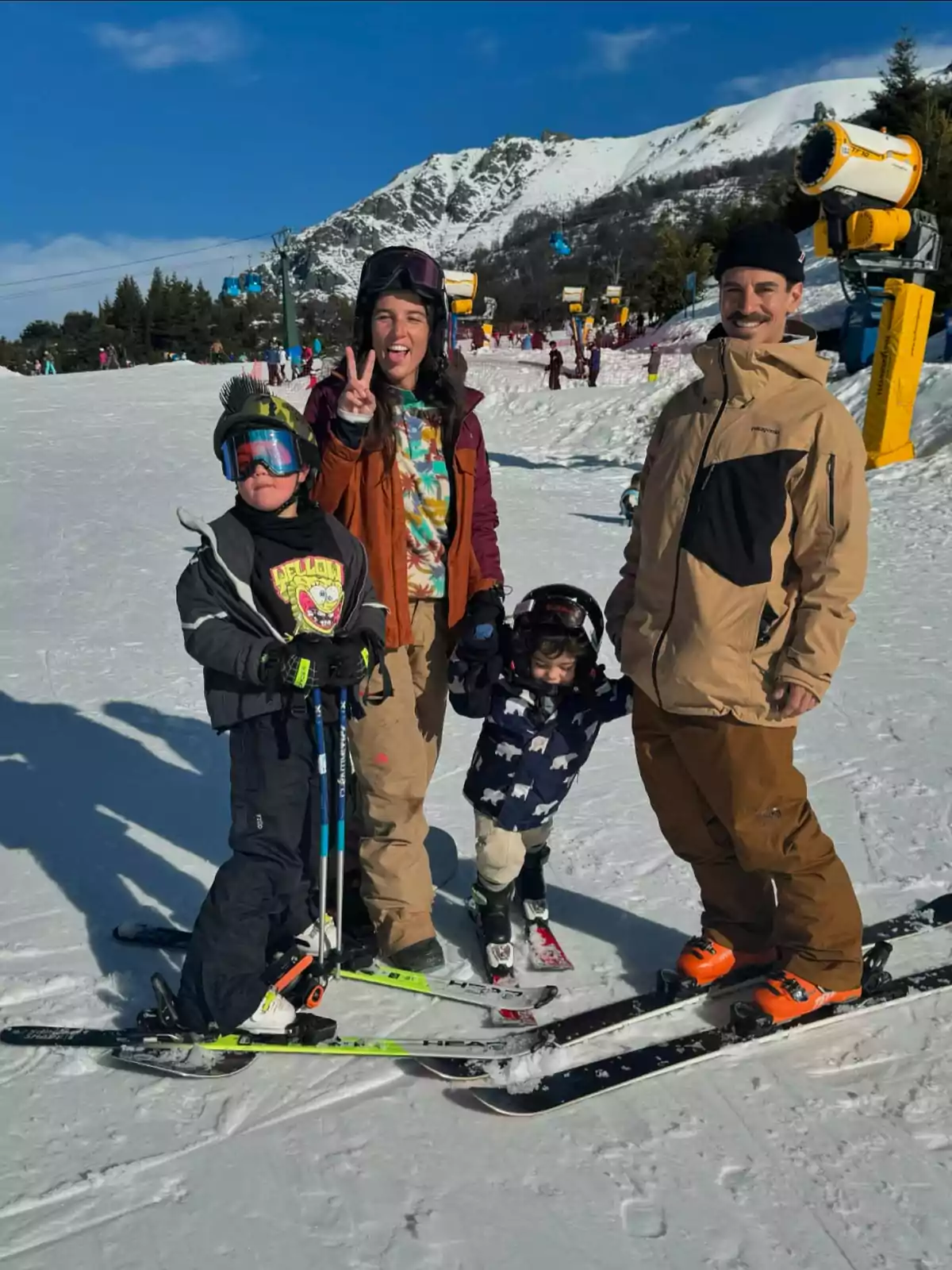 A smiling family with ski gear poses on a snowy slope with mountains in the background. A smiling family with ski gear poses on a snowy slope with mountains in the background.