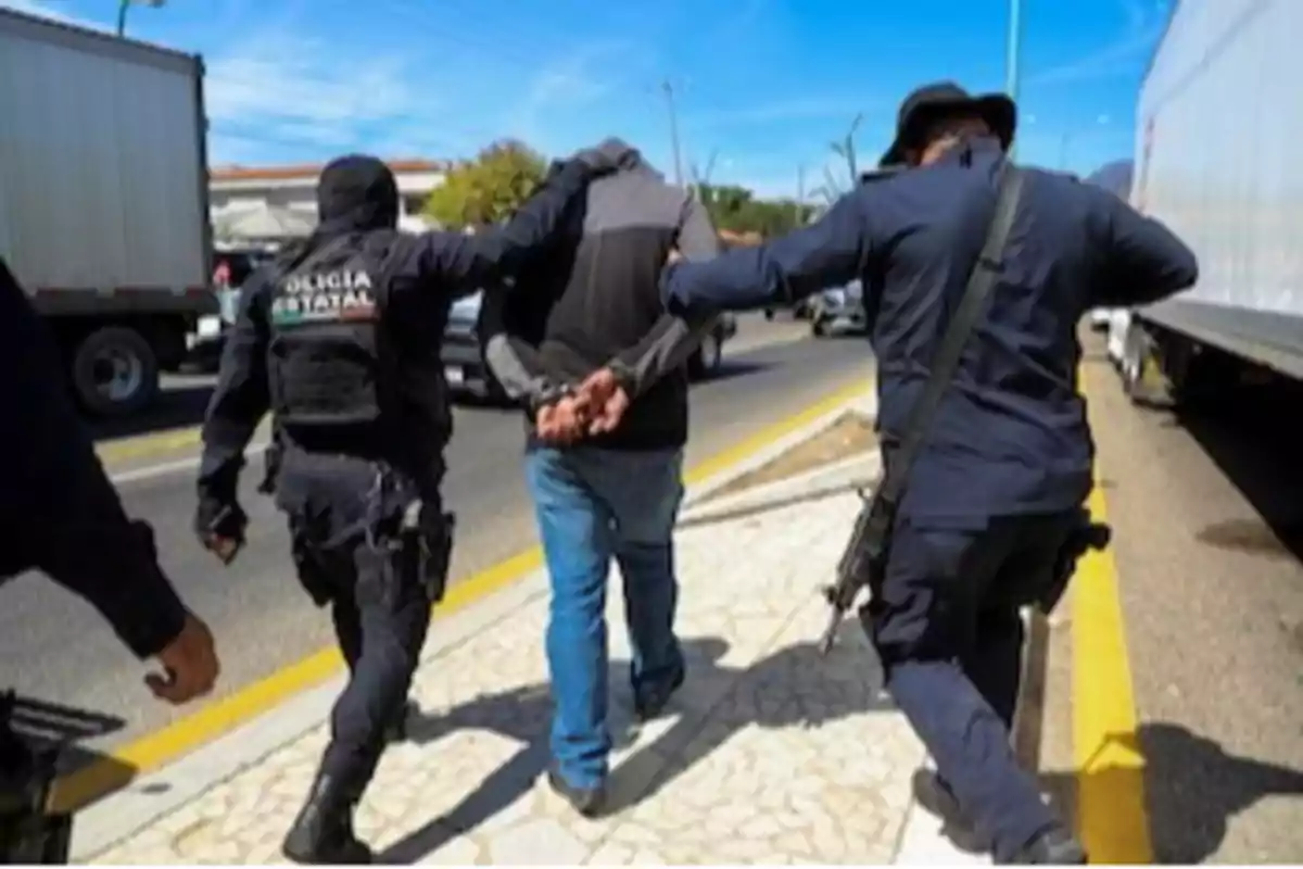 Un hombre esposado es escoltado por dos policías en una calle.