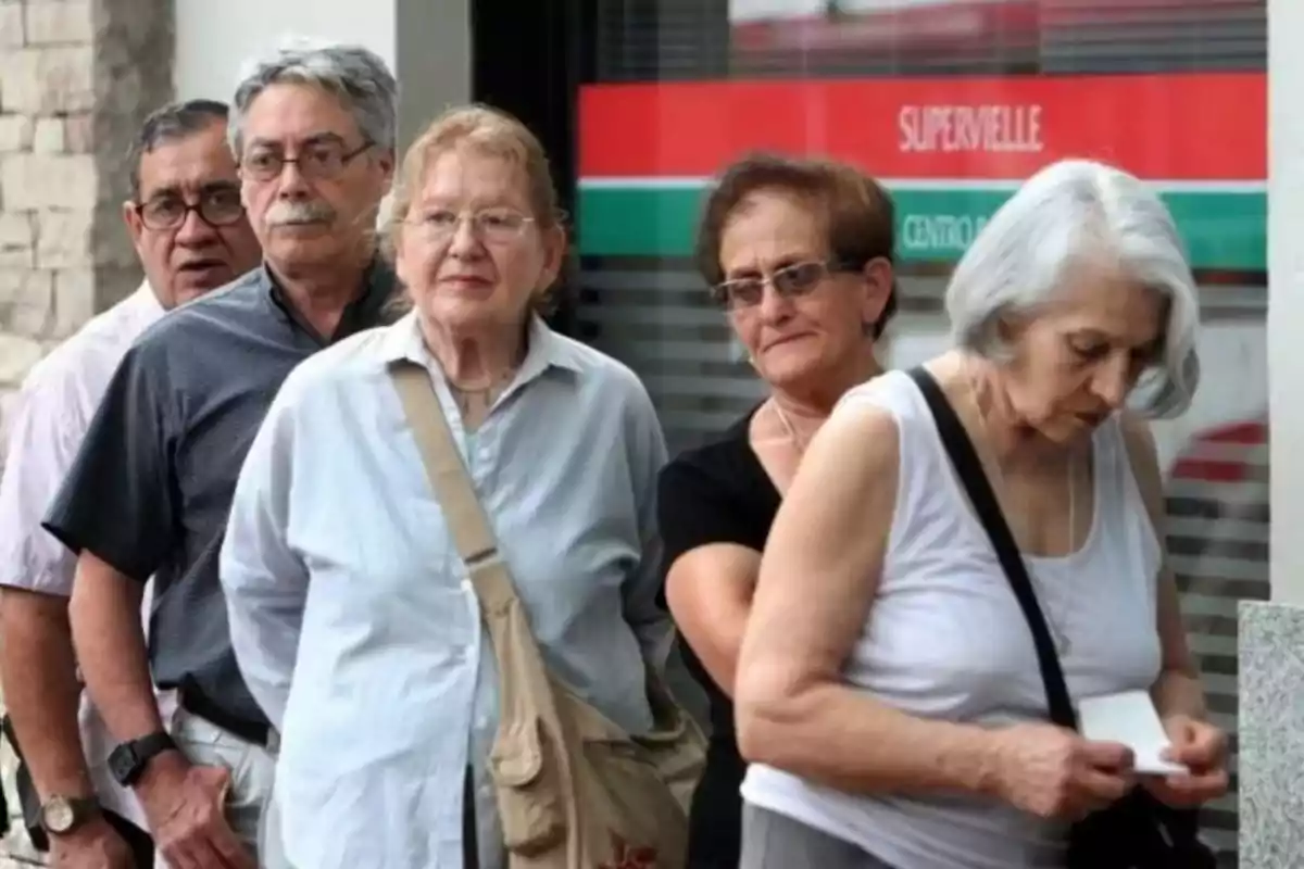 Personas mayores haciendo fila afuera de un banco.