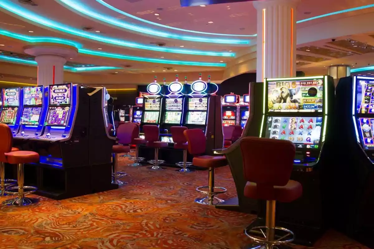 Máquinas tragamonedas en un casino con luces brillantes y sillas rojas. Máquinas tragamonedas en un casino con luces brillantes y sillas rojas.