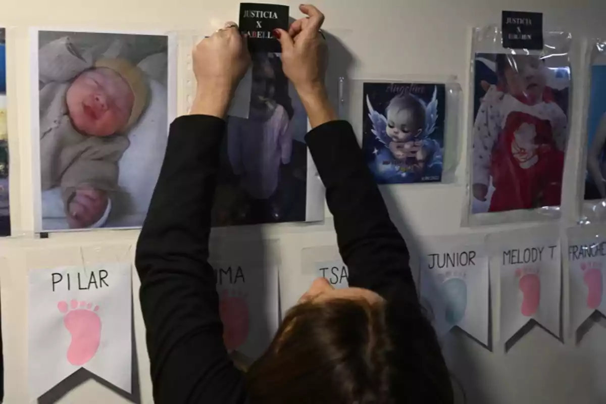 Una persona coloca un cartel en una pared donde hay fotos de bebés y niños junto a nombres y huellas de colores Una persona coloca un cartel en una pared donde hay fotos de bebés y niños junto a nombres y huellas de colores