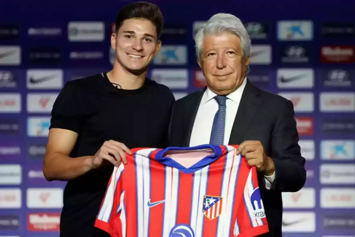 Two people pose smiling while holding an Atlético de Madrid jersey in front of a backdrop with sponsor logos. Two people pose smiling while holding an Atlético de Madrid jersey in front of a backdrop with sponsor logos.