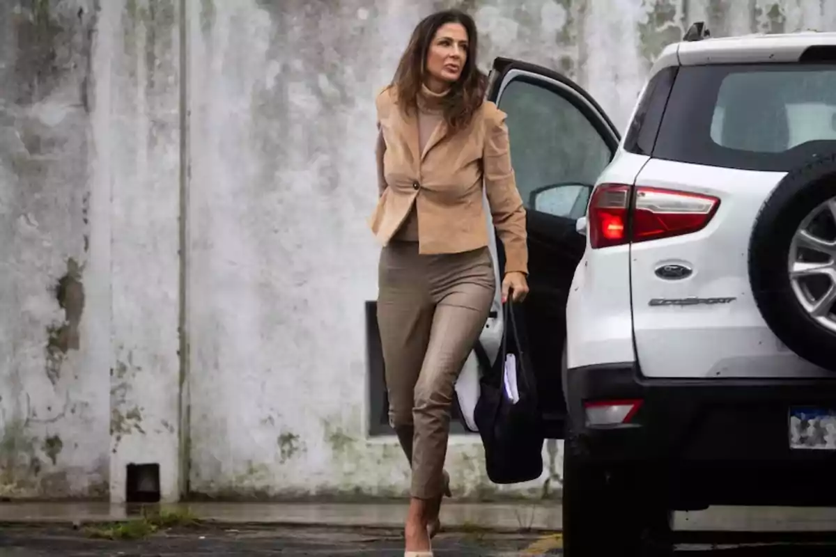 Woman dressed in beige formal attire getting out of a white SUV in front of a weathered wall