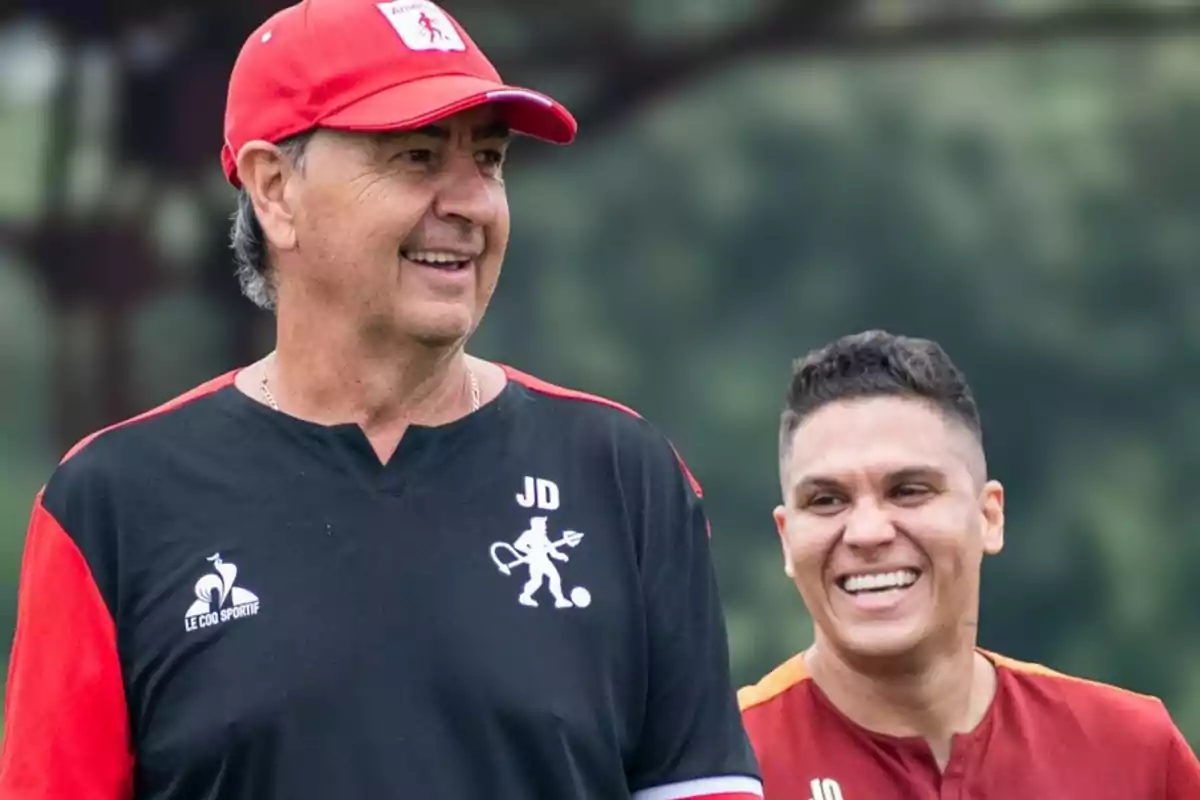Two men smile while wearing sportswear from the same team in an outdoor setting. Two men smile while wearing sportswear from the same team in an outdoor setting.