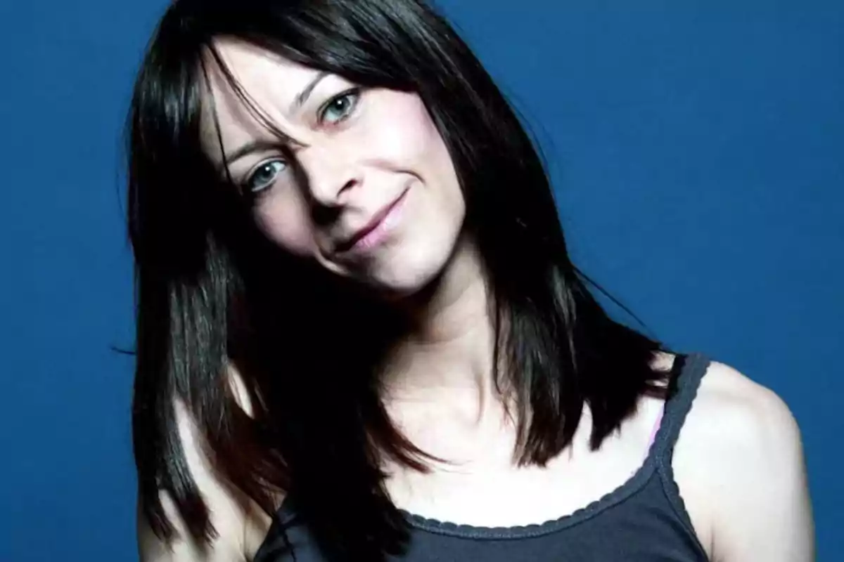 Mujer de cabello oscuro y lacio con una ligera sonrisa, posando frente a un fondo azul Mujer de cabello oscuro y lacio con una ligera sonrisa, posando frente a un fondo azul